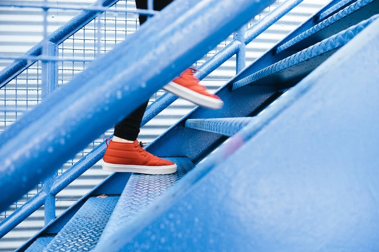 Person's feet in red sneakers walking up blue staircase