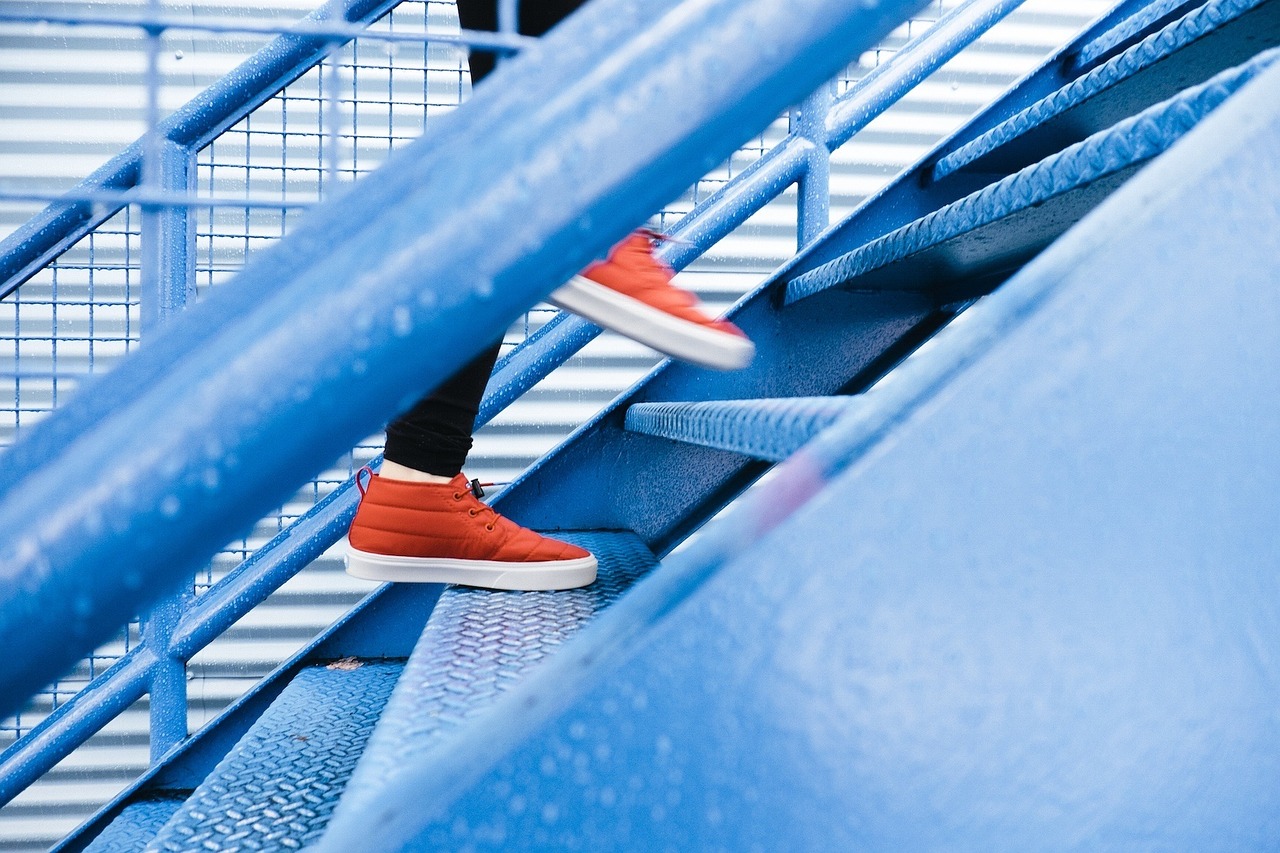 Person's feet in red sneakers walking up blue staircase