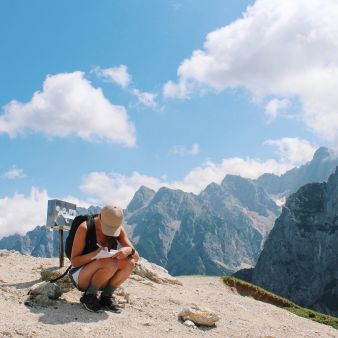 Hiker on a mountain trail crouching to write in a diary