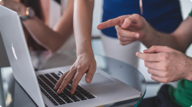 Two people are seated at a glass table, engrossed in developing a digital solution. One is pointing at the screen while the other types, embodying seamless collaboration and experience design akin to clockwork.
