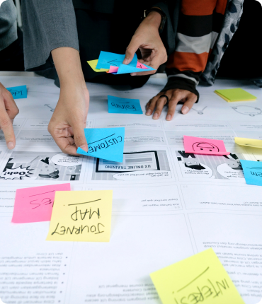 Hands arranging colorful sticky notes labeled with words like Journey Map and Customer on documents. People collaboratively planning on a white surface, enhancing the user experience through custom software solutions.