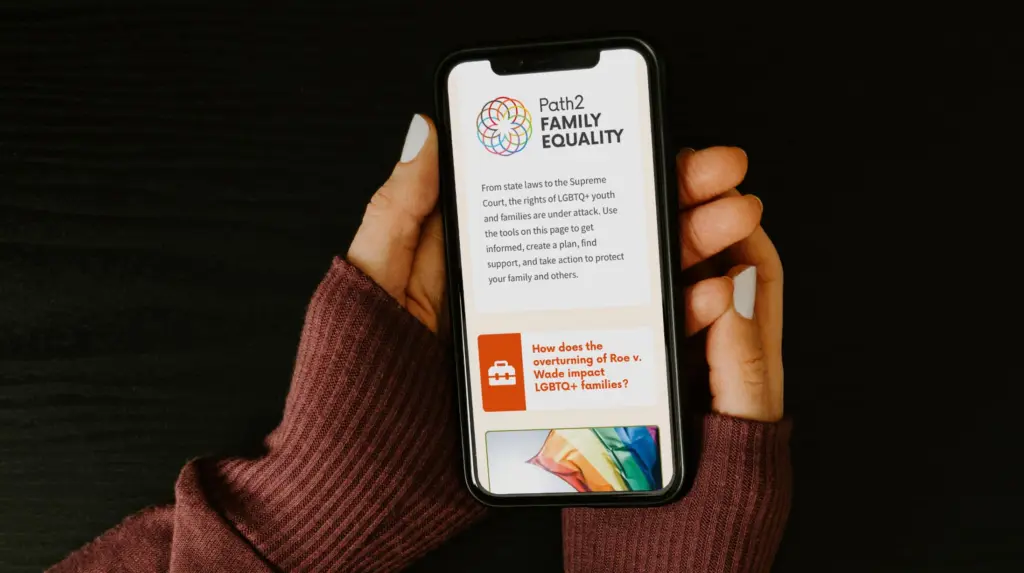 Hands holding a mobile phone with the Family Equality Path2Family Equality tool onscreen