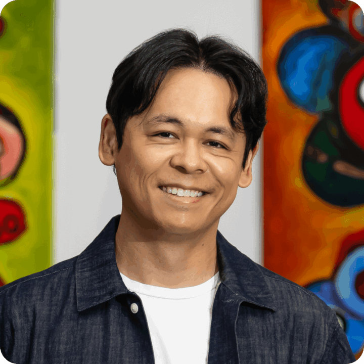Vincent Cabansag, Chief Operations Officer at Clockwork. A smiling man with dark hair wearing a white t-shirt and a dark denim jacket stands in front of colorful abstract paintings, his pose relaxed yet precise—almost clockwork in its casual confidence.