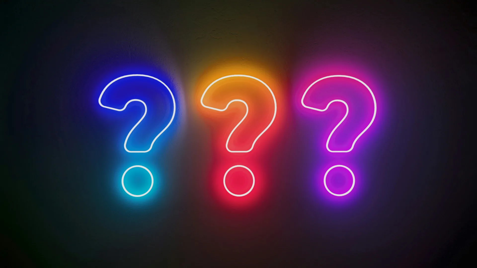 Three neon question marks in blue, orange, and pink glow brightly against a dark background, hinting at the intriguing question: what does success look like? The vibrant colors create a lively and colorful effect.