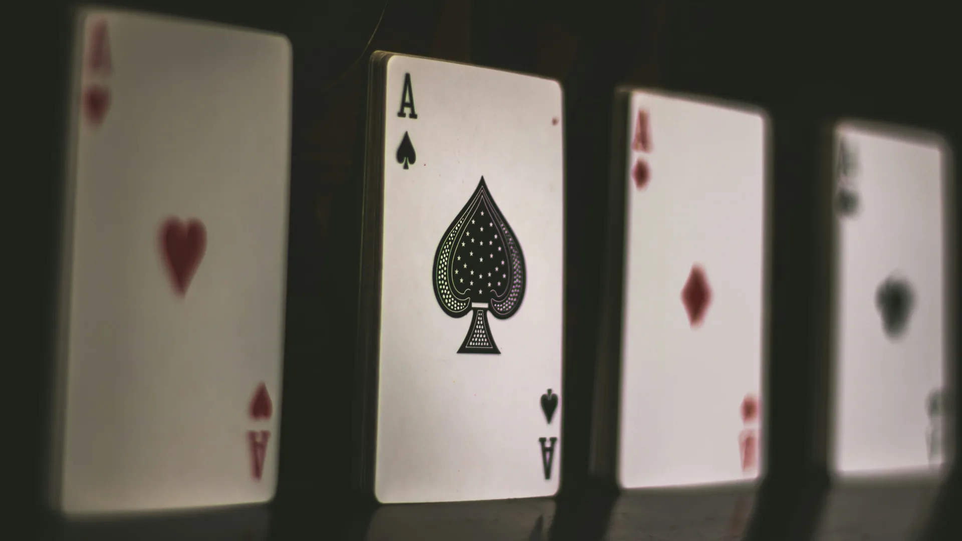 2026 digital strategy budget planning. Three playing cards are standing upright: the ace of spades in sharp focus at the center, flanked by blurred red aces (hearts and diamonds) on either side against a dark background.